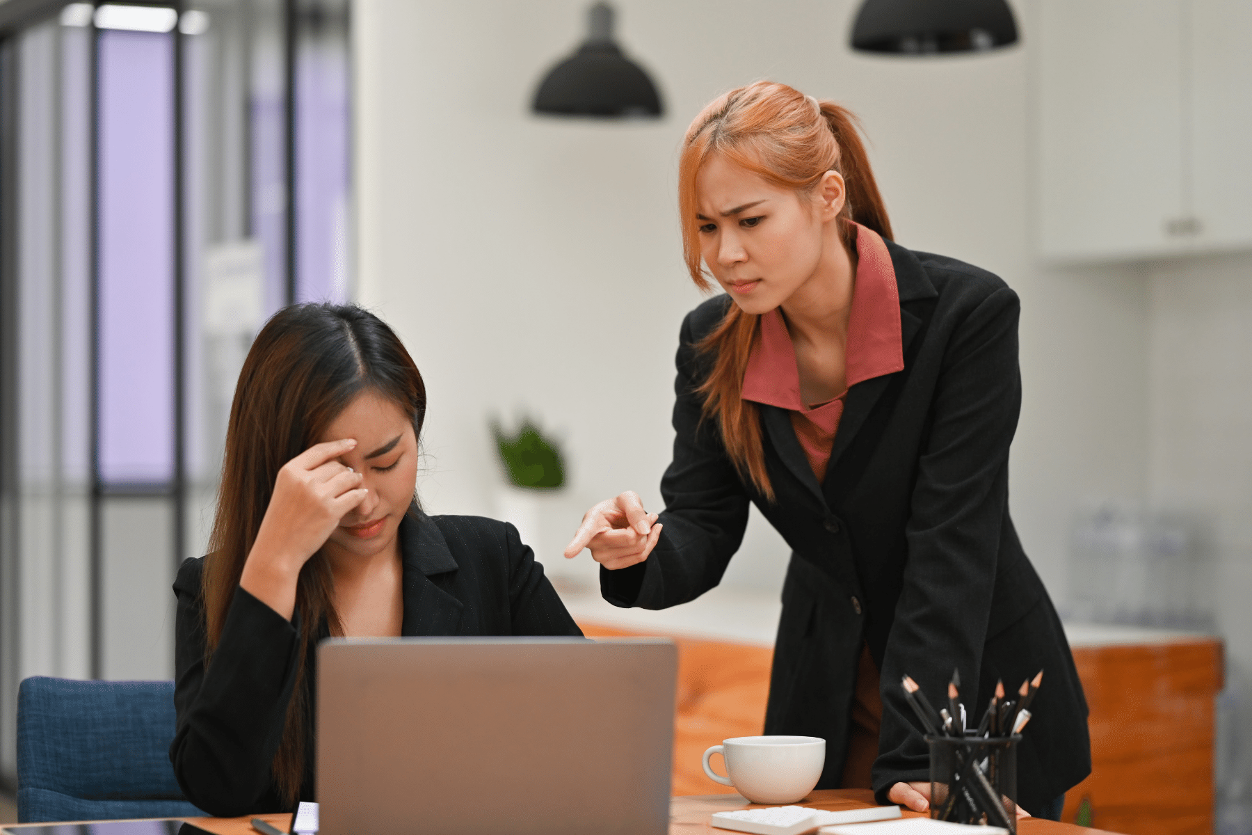 woman sitting at her laptop with her face in her hands while someone talks to her 